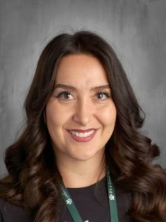 A smiling woman with long, curly hair, wearing a black shirt and green lanyard, against a gray background.