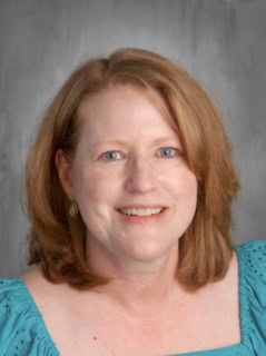 Smiling woman with medium-length brown hair, wearing a turquoise blouse, against a neutral gray background.