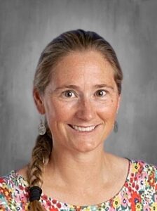 A smiling woman with a braid, wearing a colorful floral shirt, against a gray background.