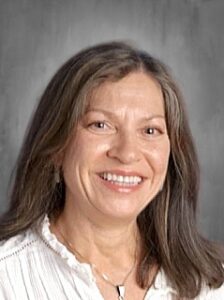 Smiling woman with long, dark hair, wearing a white blouse, against a gray background.
