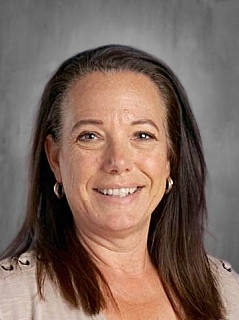 Smiling woman with long brown hair and earrings, wearing a light-colored top, against a gray background.