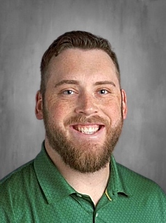 Man with short hair and beard smiling, wearing a green collared shirt against a gray background.