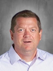 A person with short hair wearing a striped shirt against a gray background.