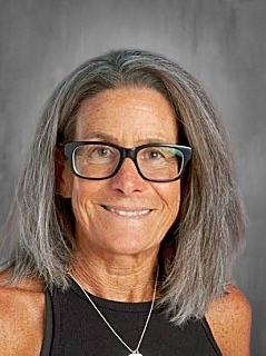 Smiling woman with gray hair and glasses, wearing a black top and necklace, against a gray background.